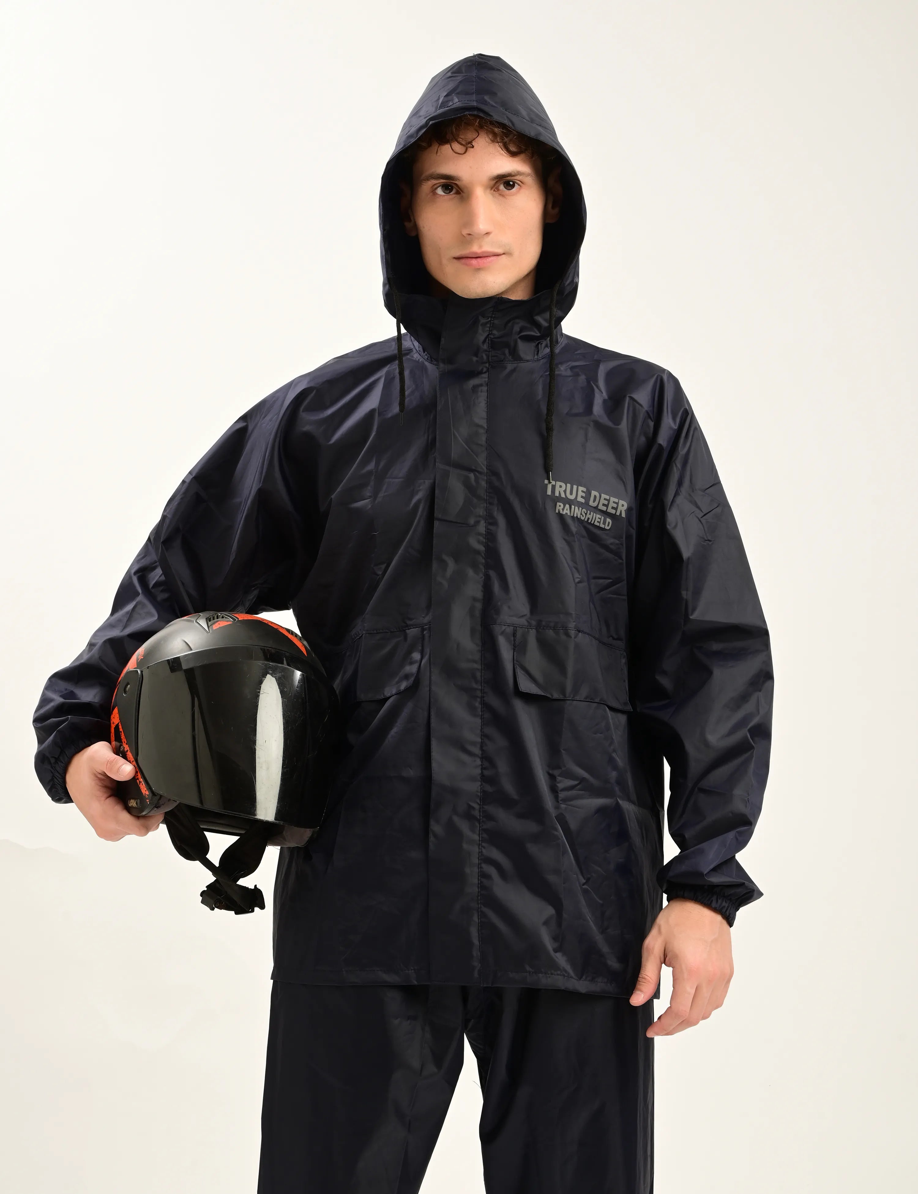 A man wearing a black waterproof hooded rain jacket and matching pants, holding a black motorcycle helmet with orange accents against a plain light background. The jacket has white text on the left chest reading 'YOUR DEEP JAWHUNTER'.